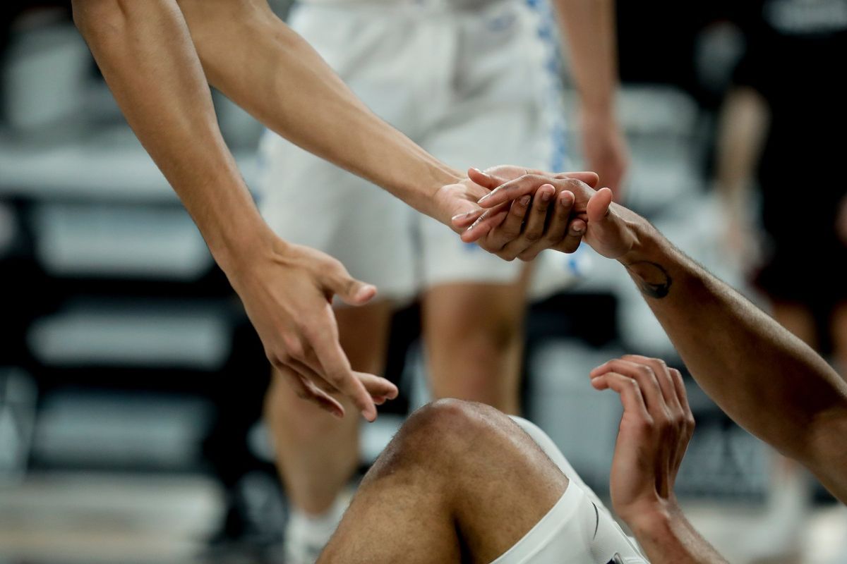 Teammates reaching down to help a basketball player back up from the court